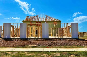 Construction of a new home with wooden frame structure under a clear blue sky, available for purchase through Jason Anson, real estate expert.